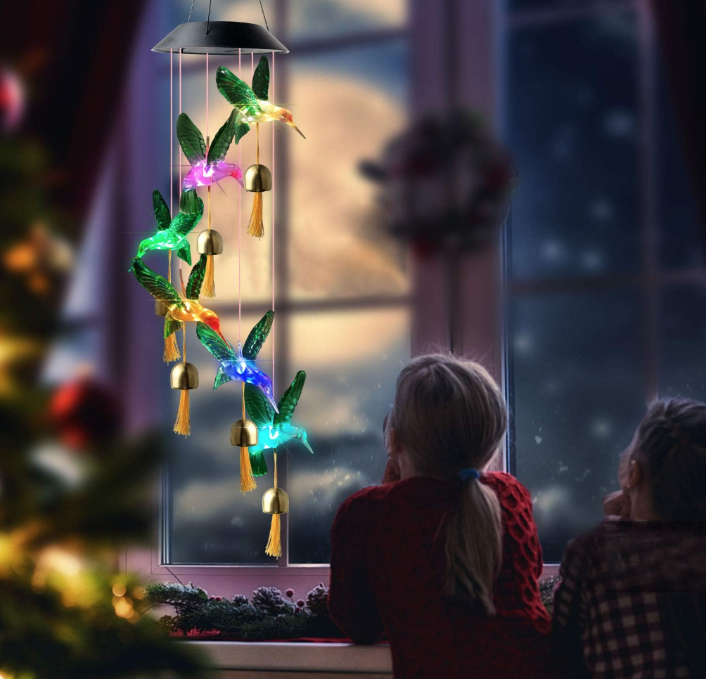 Two little girls looking at a hummingbird solar wind chime in the window of bedroom