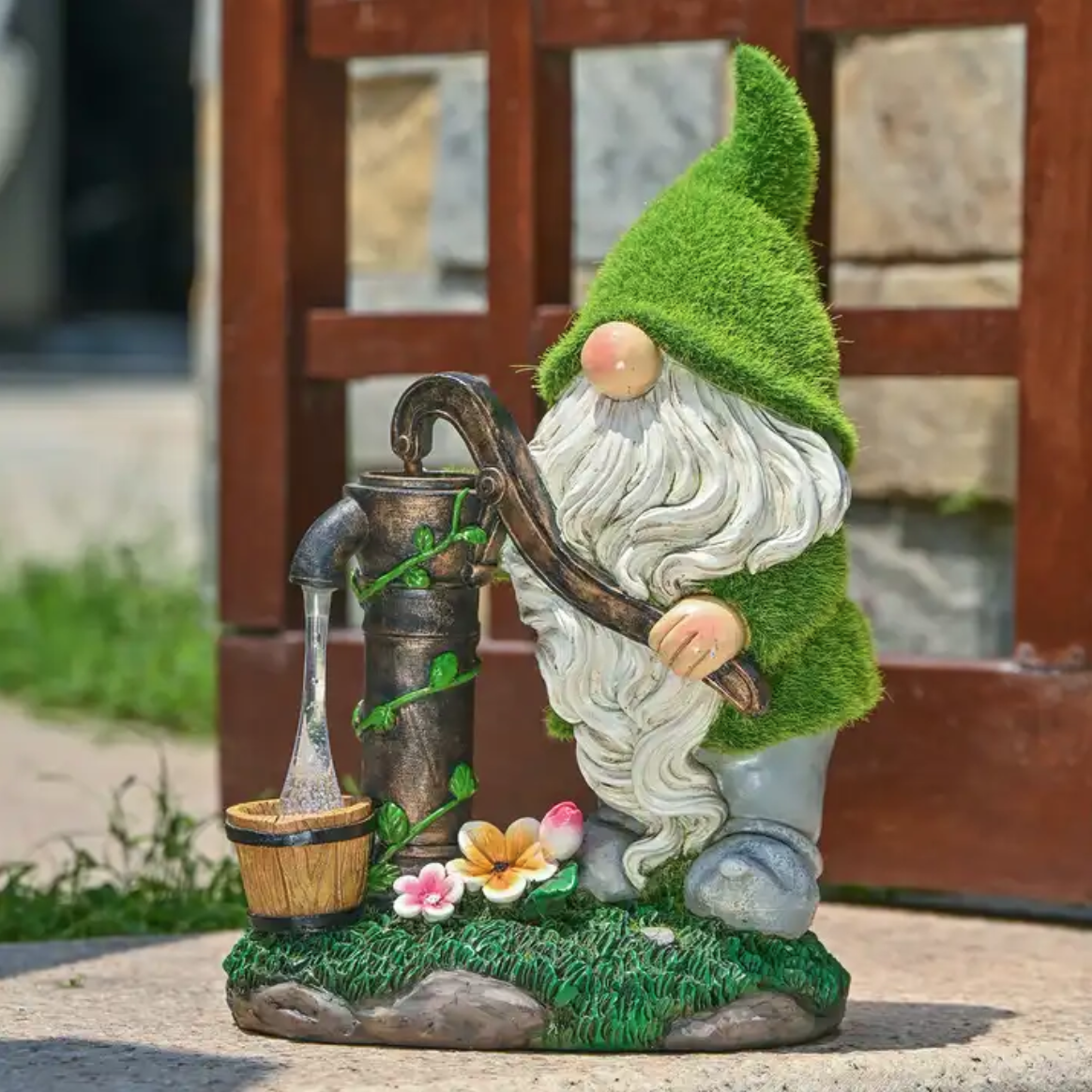 Gnome with white long beard and green flocked hat, getting water from a water pump, standing outside in a garden.
